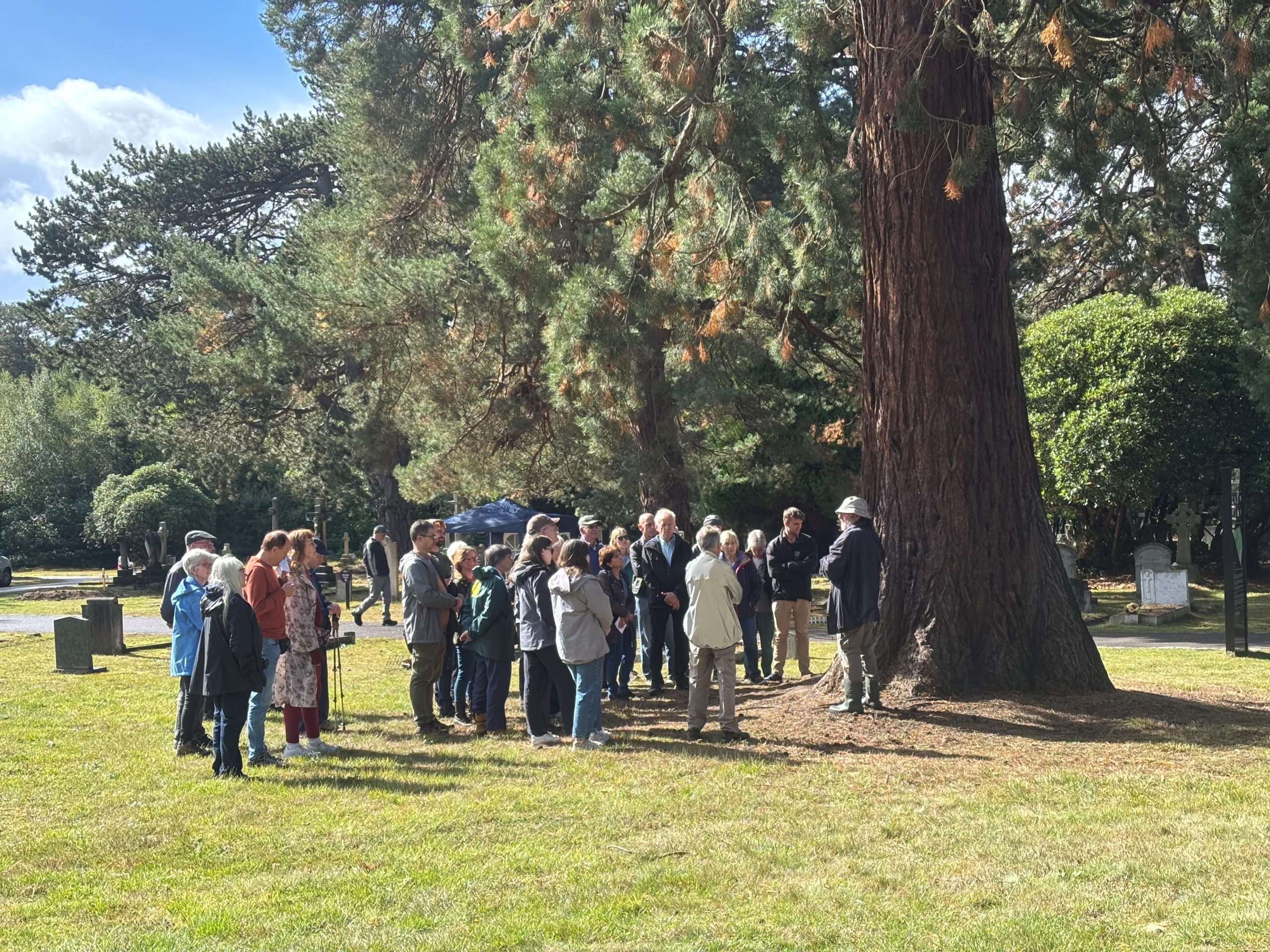 A group of 20 people gathered in the North Cemetery listening to a tour guide.