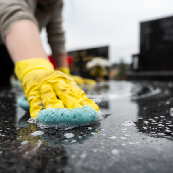 A close up on someone's hand holding a sponge whilst cleaning a marble gravestone.