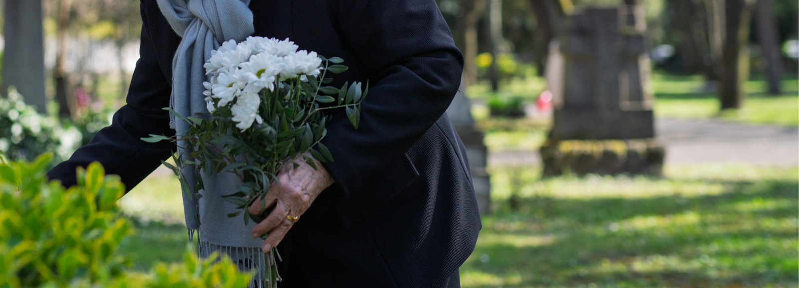 An older female placing flowers on a grave.