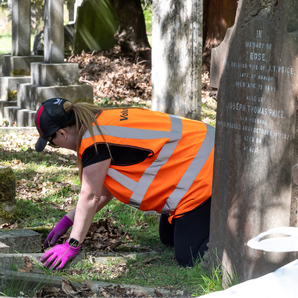 Female on her hands and knees removing leaves from a grave.