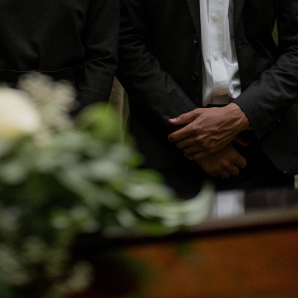Coffin in foreground, man in the background with his hands crossed.